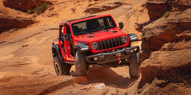 A red Jeep SUV driving off-road through a sandy, rocky desert landscape